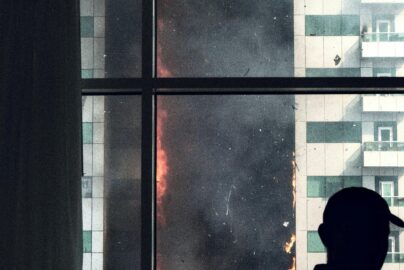 A silhouette inside observes a dramatic high-rise blaze, creating a tense and intense urban scene.