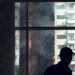 A silhouette inside observes a dramatic high-rise blaze, creating a tense and intense urban scene.